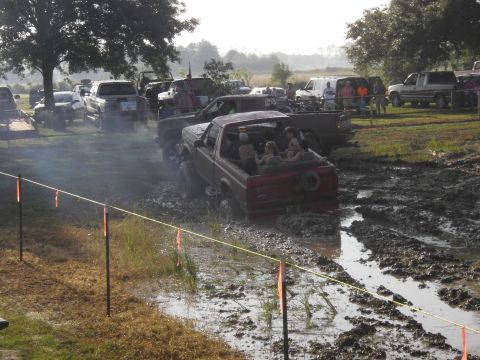 1993 Ford Bronco - Several vehicles navigate a muddy obstacle course with spectators present.