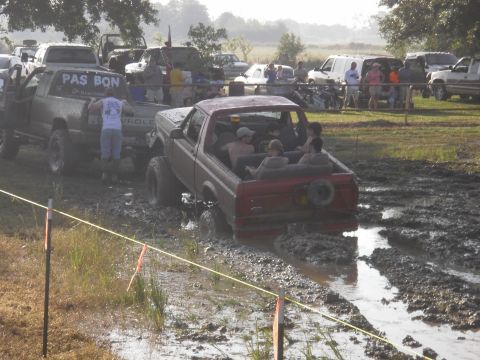 1993 Ford Bronco - A red 1993 Ford Bronco navigates a muddy track with several passengers in the open rear.