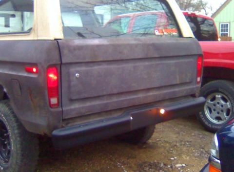 1979 Ford Bronco - Rear view of a weathered 1978 Ford Bronco with a tan soft top, parked next to a red truck.