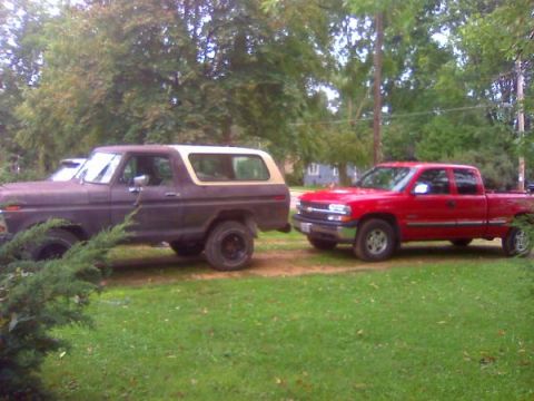 1979 Ford Bronco - Two trucks are parked side-by-side in a grassy area with trees and a house visible.