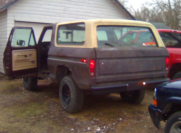 Rusty brown 1978 Ford Bronco with tan top, driver's door open, viewed from rear