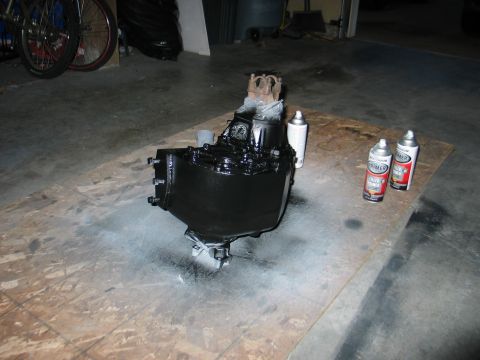 1984 Ford Bronco - A black painted transmission or transfer case sits on a plywood sheet with spray cans nearby.