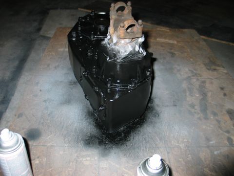 1984 Ford Bronco - Transfer case being painted black, with a rusty yoke attached. Spray cans are visible.
