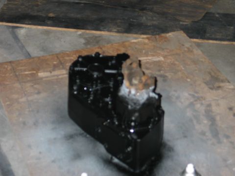 1984 Ford Bronco - A black engine part sits on a wooden surface with a concrete floor in the background.