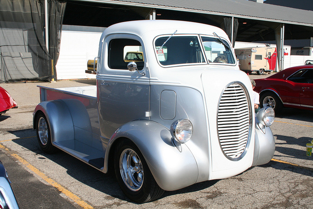 Two-tone silver and white pickup truck, front 3/4 view, custom grille, chrome wheels, visible in front of a building
