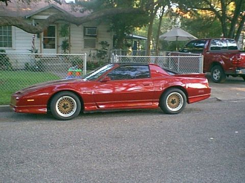 1991 Ford Bronco - A red sports coupe is parked on the street in front of a house, with a red pickup truck visible in the background.