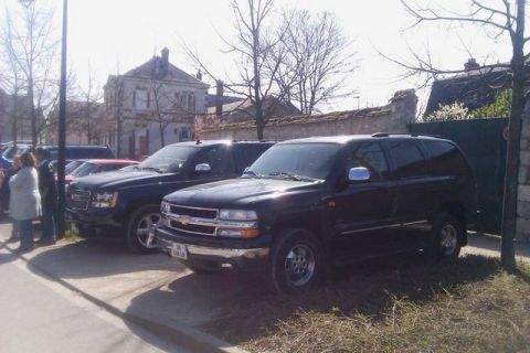 1991 Ford LTD Crown Victoria - Two dark-colored SUVs are parked on a street with buildings and trees in the background.