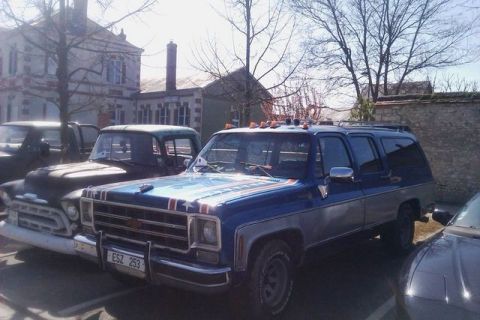 1991 Ford LTD Crown Victoria - A blue and silver Chevrolet Suburban is parked next to other vehicles, decorative stripes on its hood.
