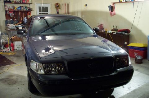 1998 Ford Crown Victoria - A dark blue sedan is parked in a garage, showing its front end with clear headlights and a black grille.