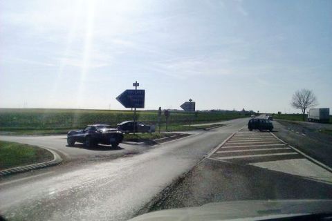 1991 Ford LTD Crown Victoria - Cars navigate an intersection on a sunny day with directional signs visible.