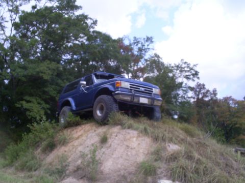 1992 Ford Bronco - Blue 1992 Ford Bronco ascends a grassy dirt mound under a cloudy sky.