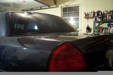 1998 Ford Crown Victoria - Rear quarter panel and taillight of a dark 1998 Ford Crown Victoria, seen in a garage.