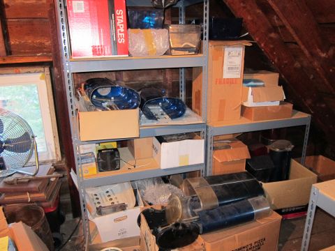 1991 Ford LTD Crown Victoria - Attic storage shelves hold various car parts, boxes, and a fan, suggesting a collection of automotive items.