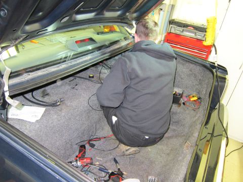 1991 Ford LTD Crown Victoria - A person works on wiring inside the trunk of a vehicle, surrounded by tools and cables.