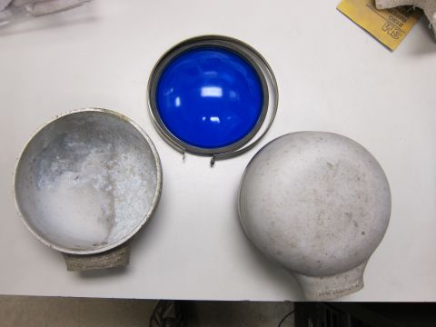 1991 Ford LTD Crown Victoria - Disassembled car headlight assembly with blue lens and two housing parts on a white surface.