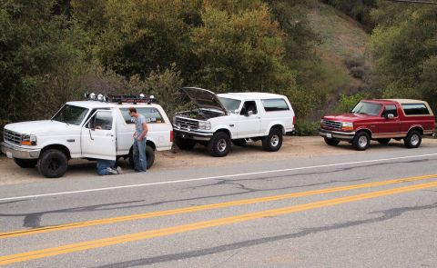 1994 Ford Bronco - Three Ford Bronco SUVs are parked roadside, with two individuals attending to one of the vehicles.