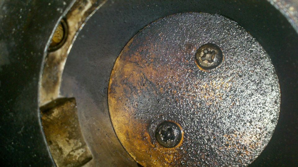 Close-up of a dirty engine cylinder with two screws visible on a circular plate