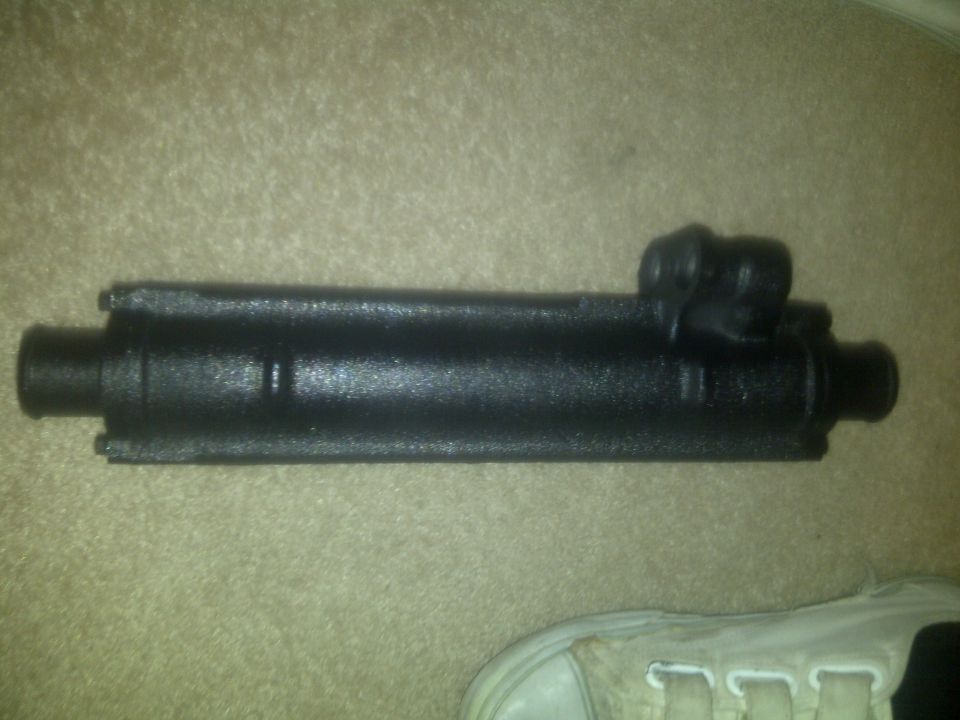 Black metal cylinder part with two fittings on one end, lying on carpet