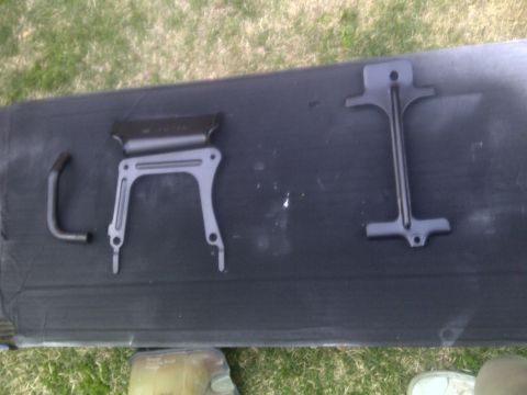 2000 Ford Crown Victoria - Three metal car parts are arranged on a dark mat, with grass visible in the background.