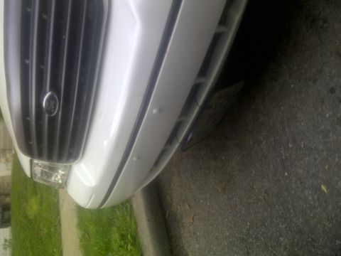 2000 Ford Crown Victoria - The front end of a white vehicle is captured, showing the grille and part of the bumper.