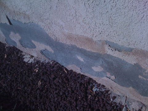 1968 Ford Mustang - Damage to a stucco wall is visible, with a layer of dark gravel at the base.