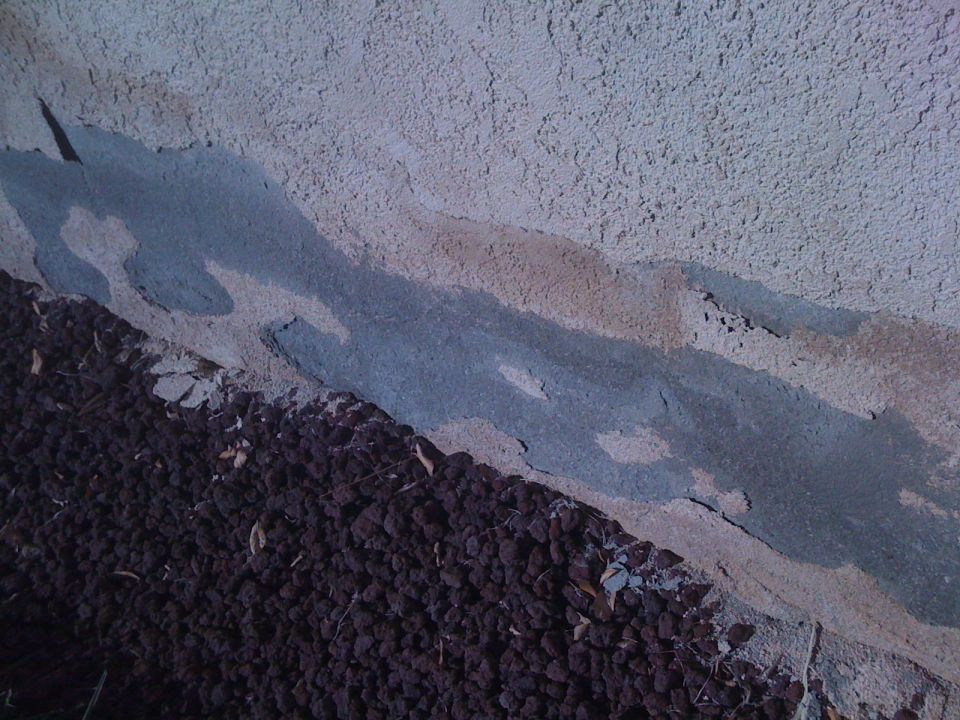 Stucco damage with dark gravel below