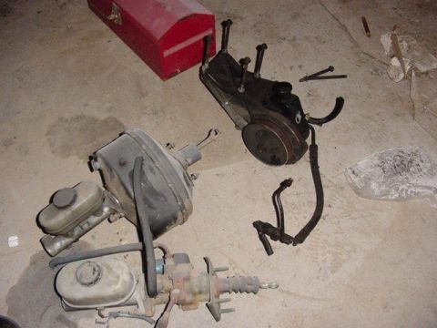 1992 Ford Bronco - Automotive brake boosters, master cylinders, and a power steering pump are laid out on a garage floor.