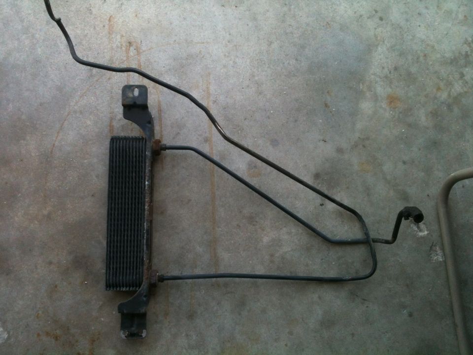 Black finned fluid cooler with bracket and long metal lines lying on concrete floor
