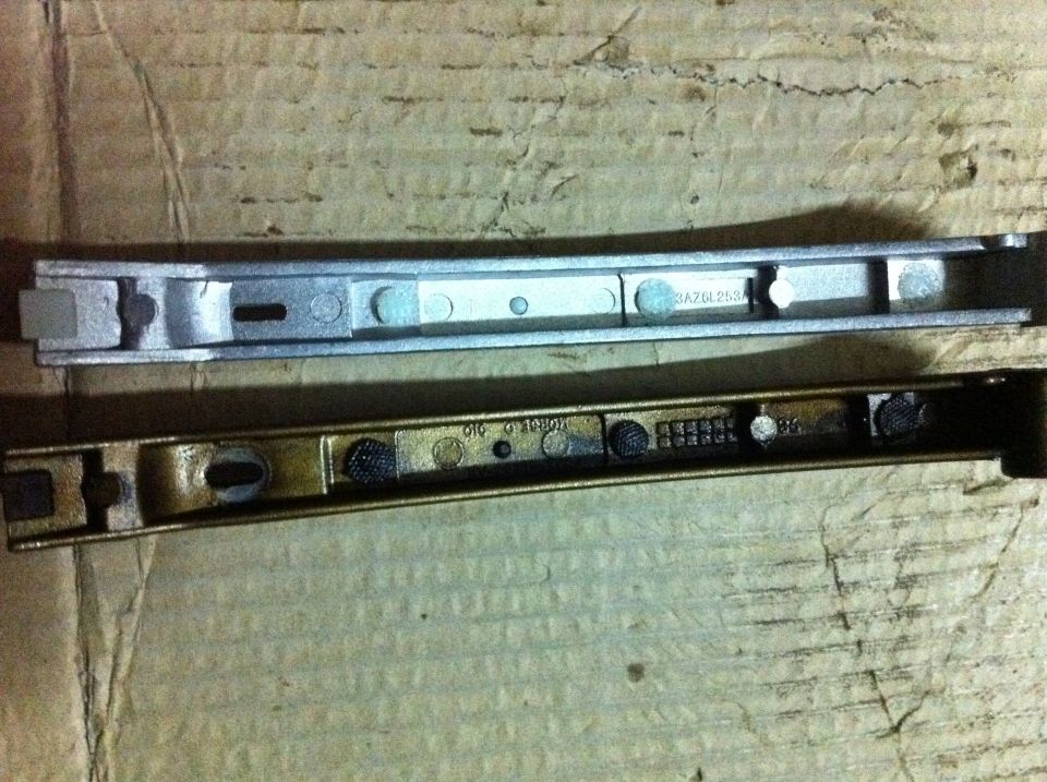 Two metal car parts, one silver and one brass, laid on a cardboard surface