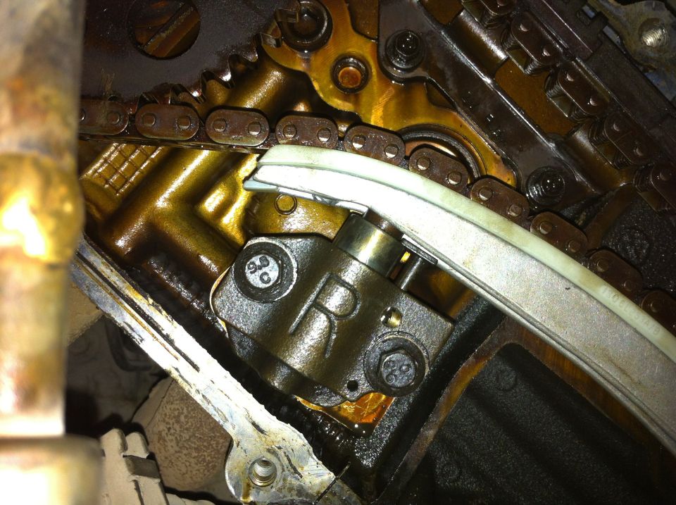 Engine timing chain and tensioner assembly with visible oil and metal components