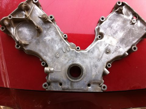 1998 Ford Crown Victoria - This is a V-shaped engine timing cover, likely made of aluminum, resting on a red surface.