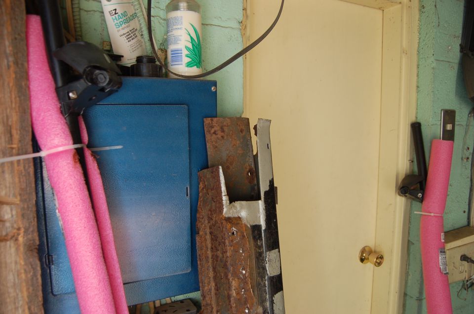 garage interior with blue electrical box, pink pool noodles, rusty metal parts, and a closed door