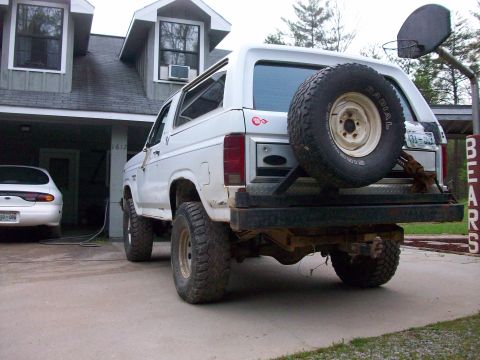 1985 Ford Bronco - The rear view of a white Ford Bronco shows its spare tire mounted on the back and a basketball hoop overhead.