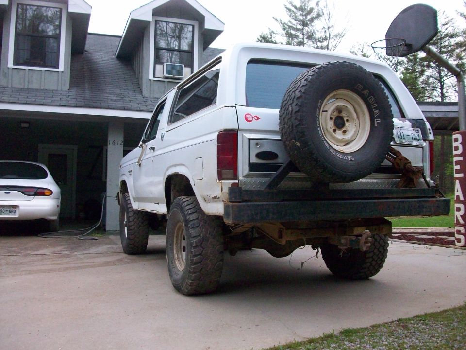 White Ford Bronco parked in front of a house, with a white sedan in the background