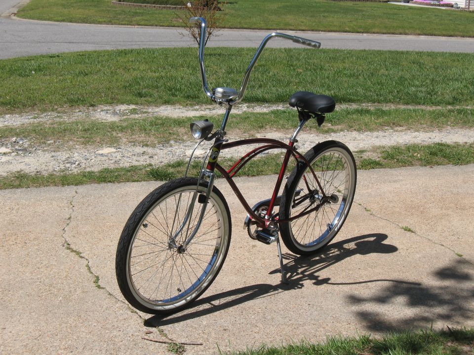 Maroon cruiser bicycle with chrome handlebars and fenders, parked on a concrete path