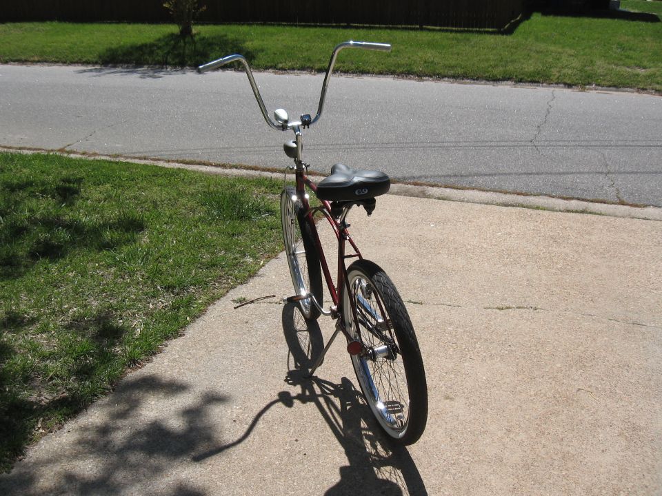 Red cruiser bicycle with ape handlebars and black seat, viewed from the rear