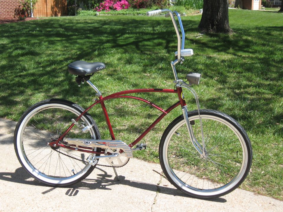Red cruiser bicycle with chrome handlebars and fenders, parked on a sidewalk