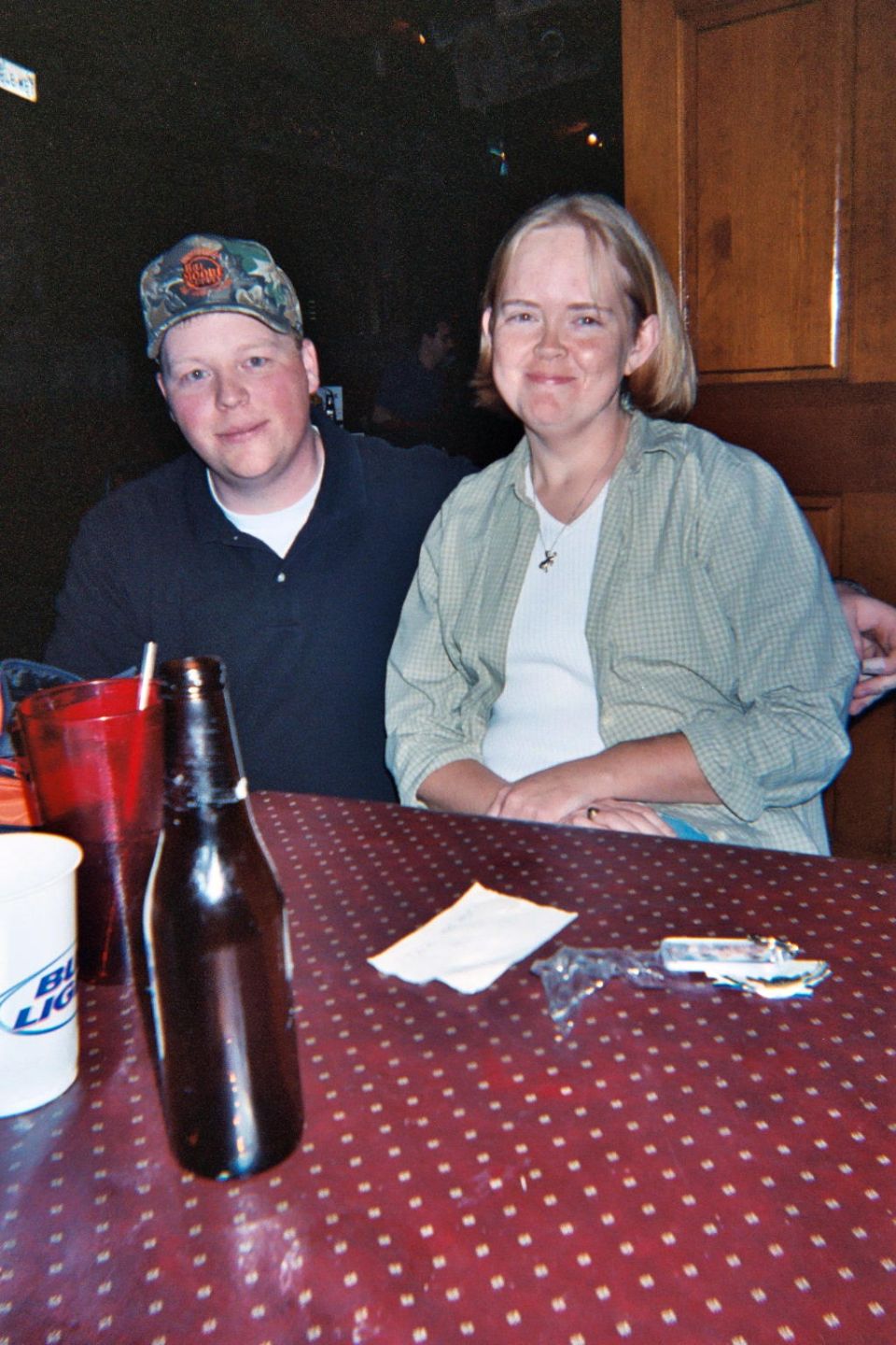 Man in a cap and woman sit at a table with a bottle and cups