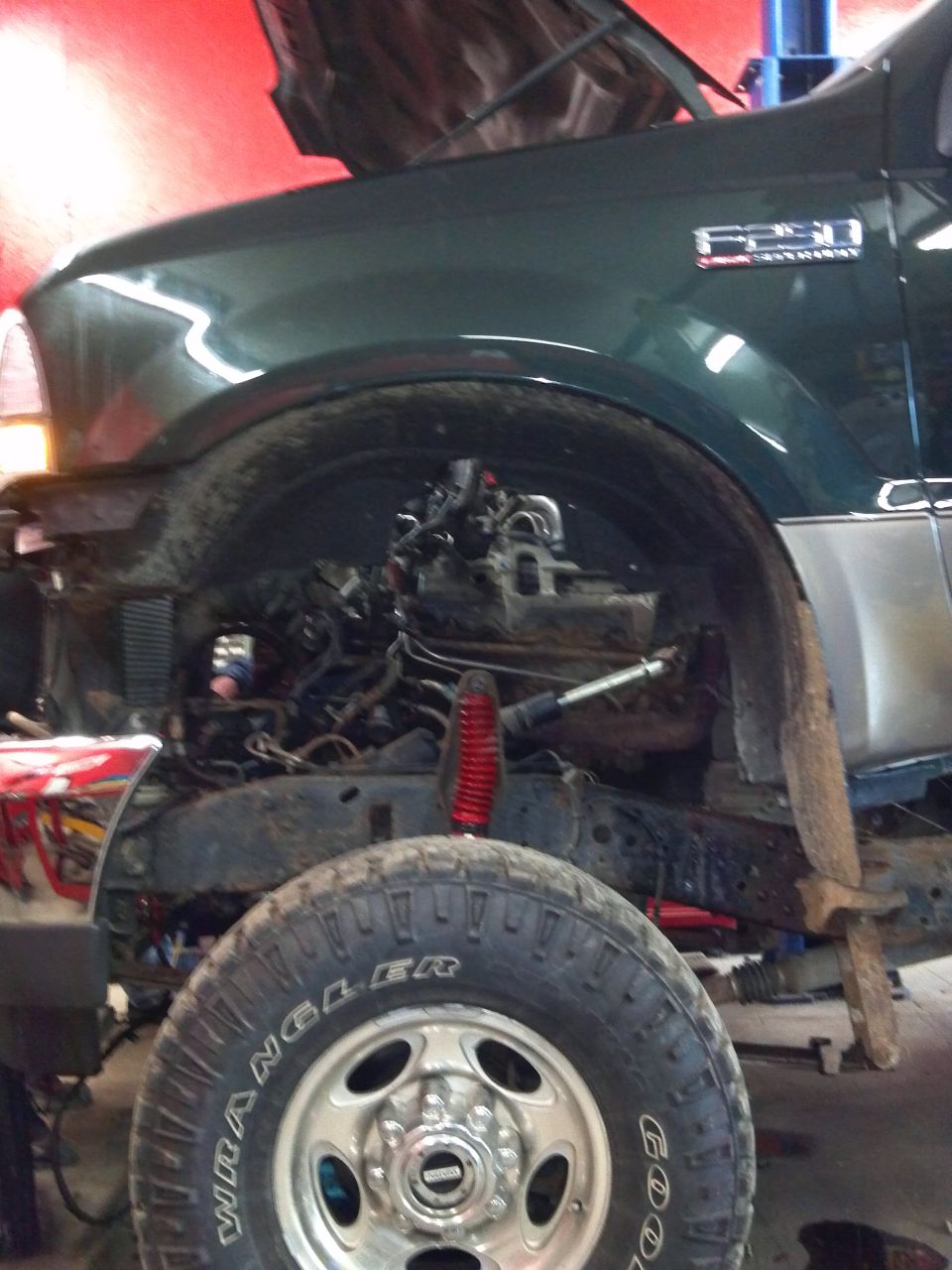 Green truck front view, hood open, engine exposed. F250 badge visible