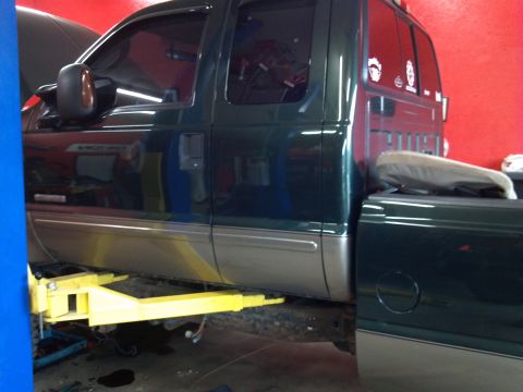 1993 Ford F-150 - A dark green pickup truck is raised on a yellow lift inside a garage, with its hood open.