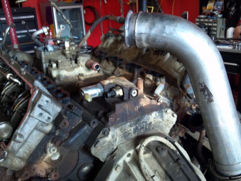 1993 Ford F-150 - Close-up view of a dirty engine with a large metal pipe attached to the exhaust manifold.