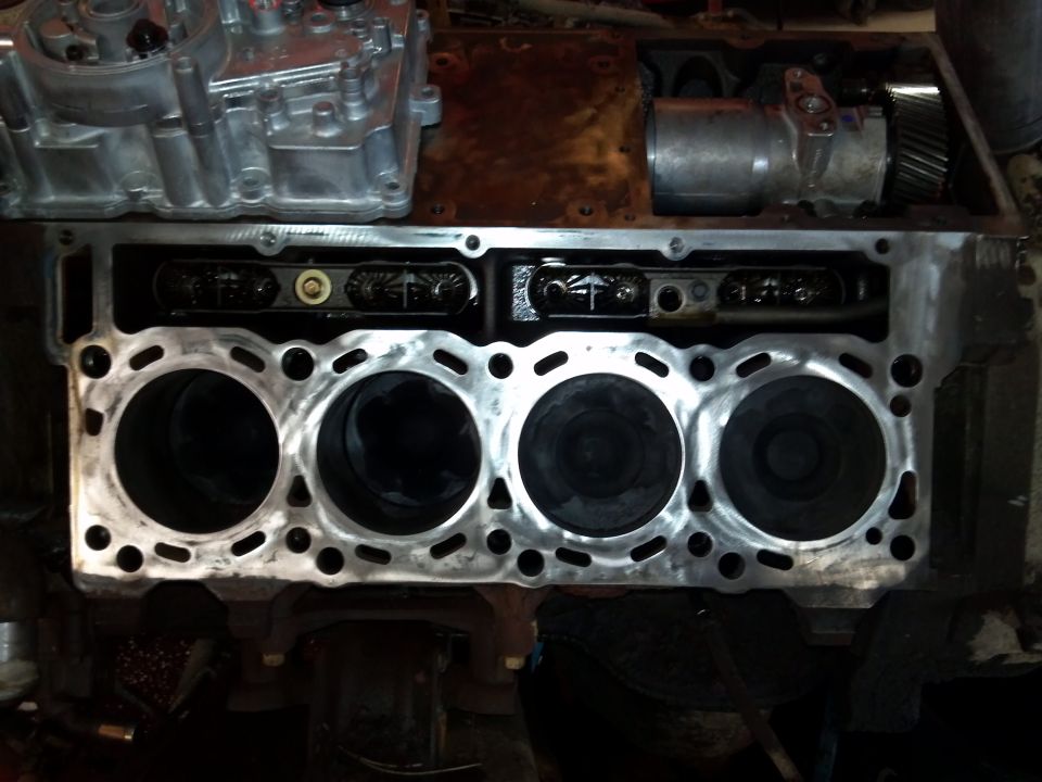 Engine block with four cylinders visible, showing pistons and part of the engine assembly