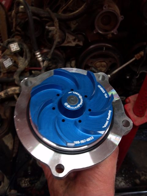 1993 Ford F-150 - A blue performance water pump is held in a hand, with engine components visible in the background.