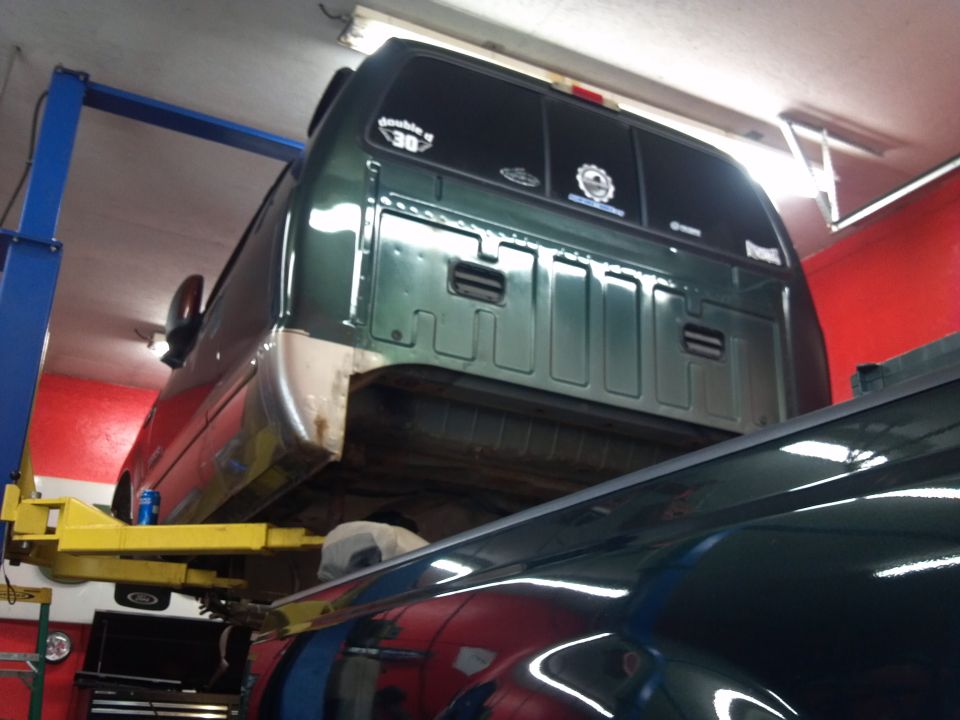 Green pickup truck bed and cab on a lift, with another vehicle below
