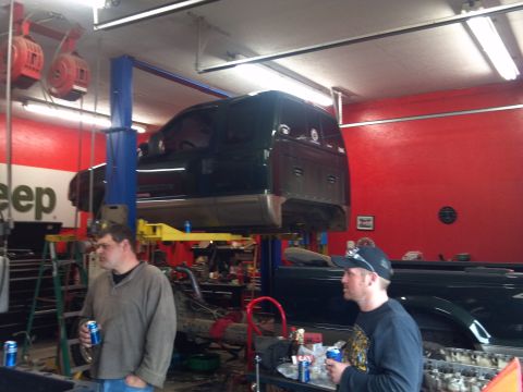 1993 Ford F-150 - Two men stand in a garage as a dark pickup truck is raised on a lift, with another truck visible in the background.