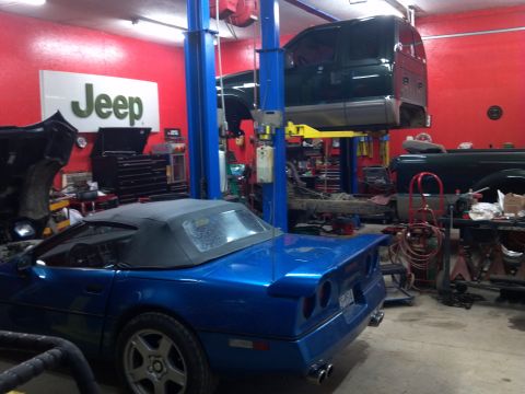 1993 Ford F-150 - A blue convertible sports car is parked in a garage with a Jeep sign on the wall and another vehicle on a lift.