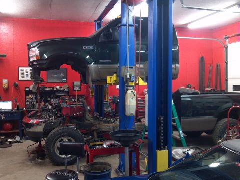 1993 Ford F-150 - A green Ford truck is undergoing repairs on a lift in a garage; another truck is parked behind it.