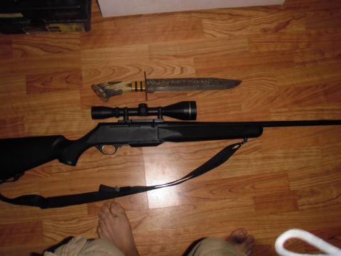 1993 Ford Bronco - A rifle and a hunting knife are laid out on a wooden floor, with a partial view of a person's legs and feet.