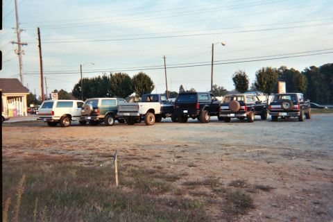 1988 Ford Bronco - Several Ford Broncos and a pickup truck are parked in a lot under a partly cloudy sky.