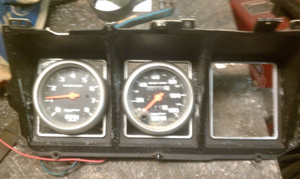 Dashboard gauge cluster with tachometer, speedometer, and empty slot. Orange needles on black faces